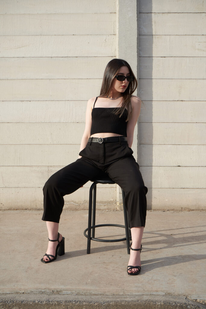 Gabriela Inzunza for Avice a stylish pose against a minimalist backdrop showcasing a monochrome ensemble with a sleek belt and heels.
